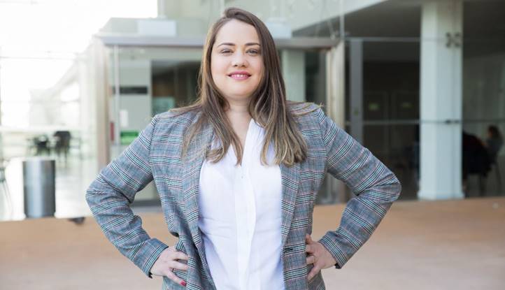Vrouw in blazer poseert zelfverzekerd buiten voor een modern kantoorgebouw