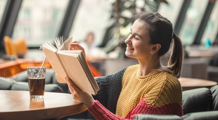 Vrouw leest glimlachend een boek in een café met een glas frisdrank op tafel