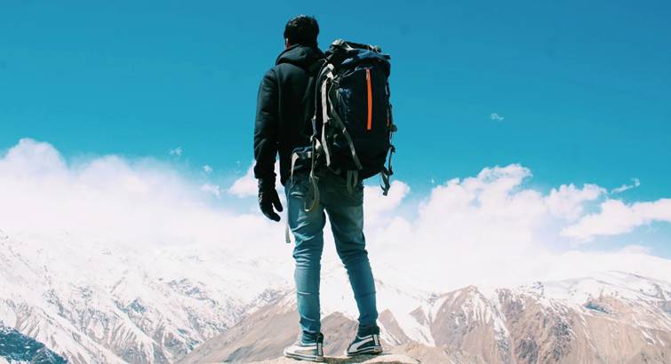 Backpacker staat met uitzicht over besneeuwde bergen, symbool voor reizen zonder vast plan.