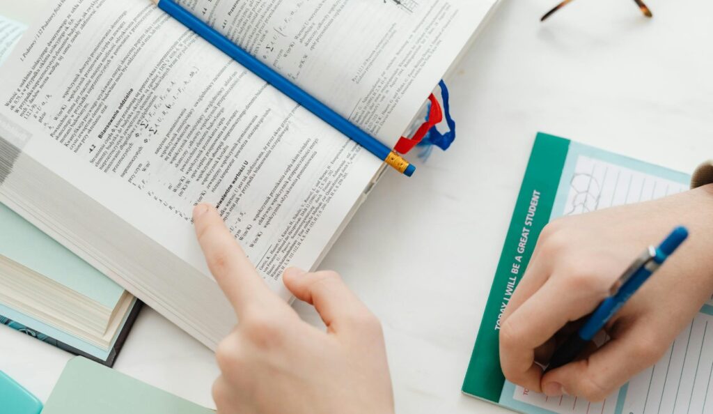 Student wijst in studieboek met formules terwijl hij aantekeningen maakt voor beter begrip en voorbereiding.