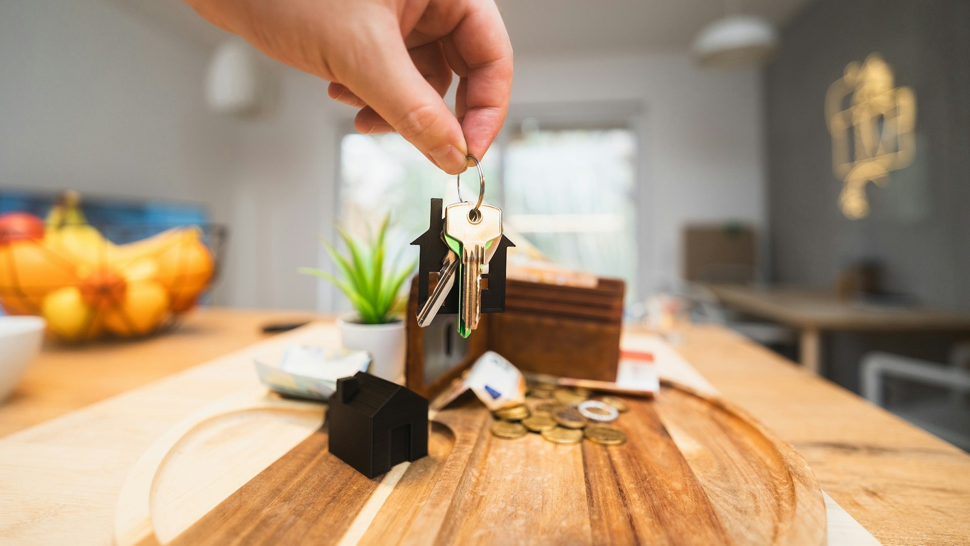 Sleutels van nieuwe woning in hand tijdens verhuizen met miniatuurhuis en geld op tafel