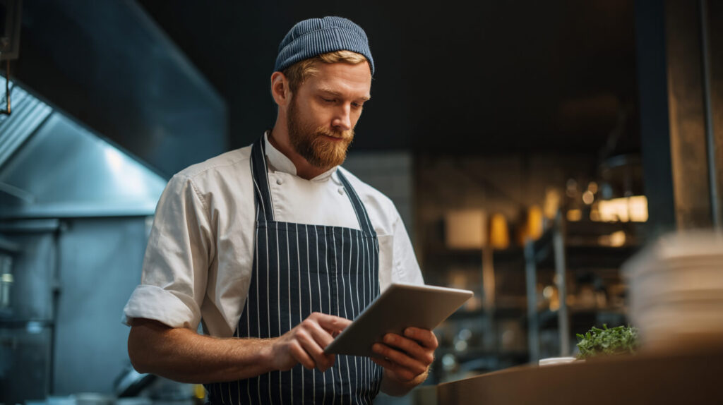 Een kok checkt bestellingen en omzetgegevens op een tablet in de horecakeuken